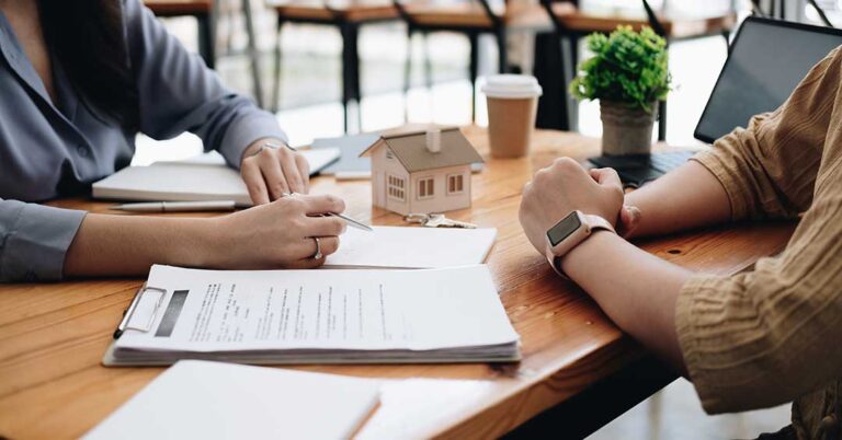 A couple reviews paperwork with a real estate folder and keys in a bright, welcoming home environment.